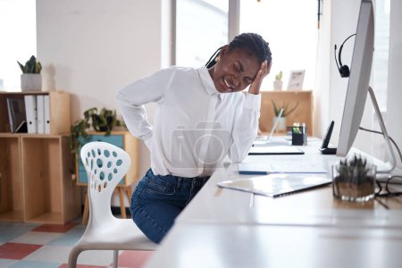 Foto de Puede que se haya excedido demasiado. una joven mujer de negocios que experimenta dolor de espalda mientras trabaja en su escritorio en una oficina moderna - Imagen libre de derechos