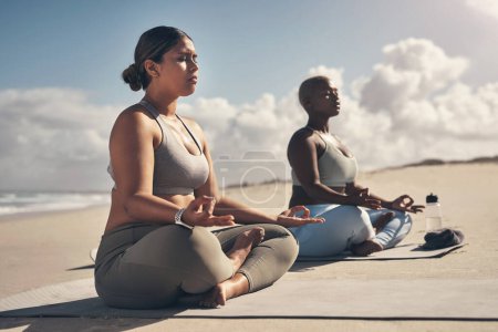 Téléchargez les photos : Yoga vous aide à devenir une meilleure version de vous-même. deux jeunes femmes méditant pendant leur routine de yoga sur la plage - en image libre de droit