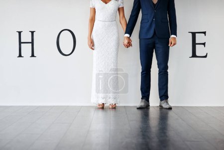 Téléchargez les photos : Ce sont nos premiers pas. Concept studio plan d'une mariée et d'un marié faisant un M dans le mot maison contre un mur - en image libre de droit
