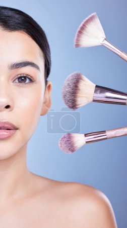 Photo for Studio Portrait of a beautiful mixed race woman posing with a collection of makeup brushes during pamper routine. Hispanic model with cosmetic tools standing against a blue copyspace background. - Royalty Free Image