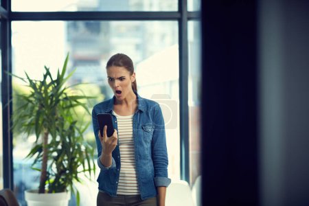 Téléchargez les photos : Tu te fous de moi ? une jeune femme d'affaires utilisant un téléphone portable et regardant en colère dans un bureau moderne - en image libre de droit