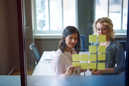Téléchargez les photos : Cette équipe regorge de nouvelles idées. deux femmes d'affaires brainstorming avec des notes adhésives sur un mur de verre dans un bureau - en image libre de droit