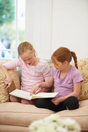 Foto de Usando su imaginación. Dos hermanas leyendo un cuento en el salón - Imagen libre de derechos