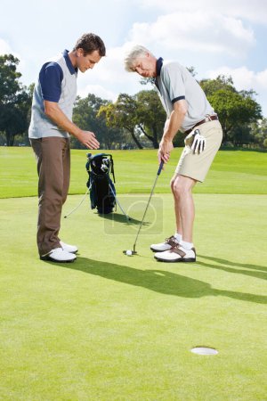 Téléchargez les photos : Maintenant, essayez de garder une ligne droite... deux hommes jouant une partie de golf ensemble sur le green - en image libre de droit