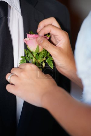 Photo for Its in the details. Closeup of a bride adjusting the pink rose on her husbands jacket - Royalty Free Image