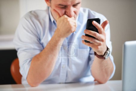 Das kann nicht gut sein... ein müde aussehender Geschäftsmann liest eine SMS, während er vor seinem Laptop sitzt