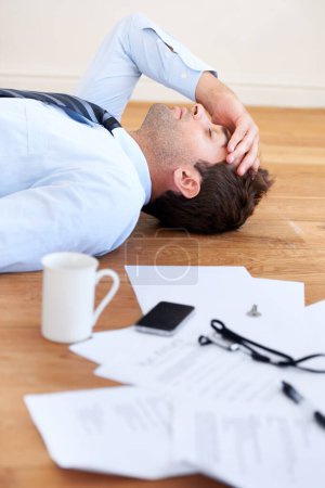 Photo for Collapsing under the pressure. A businessman lying on the floor with hand rested on his head and paperwork lying on the floor in front of him - Royalty Free Image