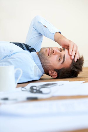 Photo for Hes over his head in paperwork. Portrait of a businessman lying on the floor with his hand rested on his head and paperwork lying on the floor in the foreground - Royalty Free Image