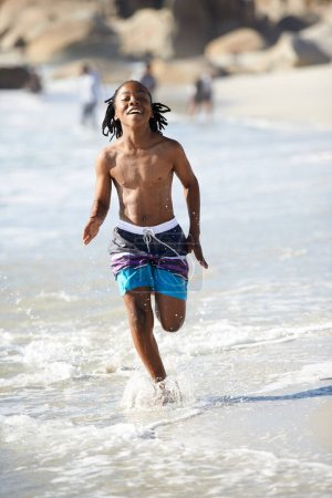 Téléchargez les photos : Charger à travers le surf. Un jeune garçon excité chargeant dans les eaux peu profondes de la mer - en image libre de droit