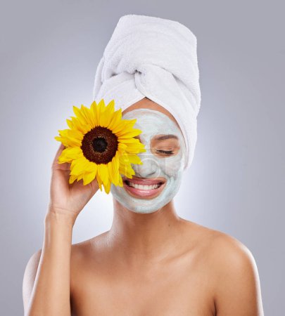 Foto de Diviértete mientras cuidas tu piel. una atractiva joven con una máscara facial y sosteniendo un girasol sobre su ojo en el estudio - Imagen libre de derechos