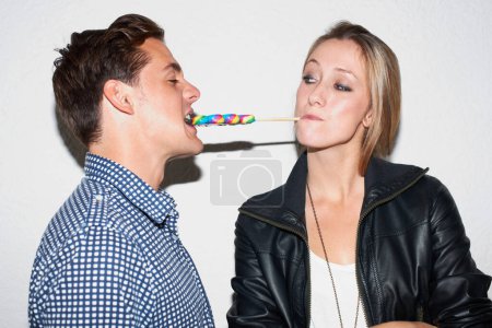 Photo for Sharing a sweet moment. Young hipster woman feeding her boyfriend a striped lollipop - Royalty Free Image