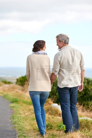 Photo for Having a leisurely stroll. A couple holding hands walking along the road - Royalty Free Image
