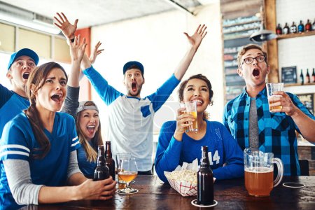 Téléchargez les photos : Il n'y a pas de temps comme le jeu. un groupe d'amis qui applaudissent en regardant un match de sport dans un bar - en image libre de droit