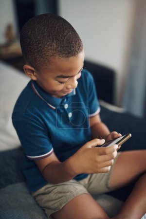 Foto de Su teléfono está configurado para requerir aprobación antes de descargar cualquier aplicación. un niño usando un celular mientras está sentado en su cama - Imagen libre de derechos
