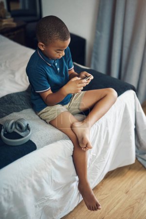 Foto de Hay muchas cosas divertidas y educativas que hacer en línea. un niño usando un celular mientras está sentado en su cama - Imagen libre de derechos