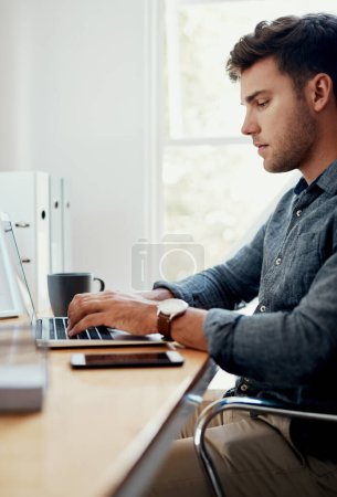 Téléchargez les photos : Un jour de plus pour atteindre ses objectifs. un beau jeune homme d'affaires assis seul et utilisant son ordinateur portable dans le bureau - en image libre de droit