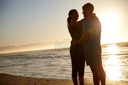 Foto de Romance temprano en la mañana. una pareja abrazada silueta contra un amanecer sobre el mar - Imagen libre de derechos