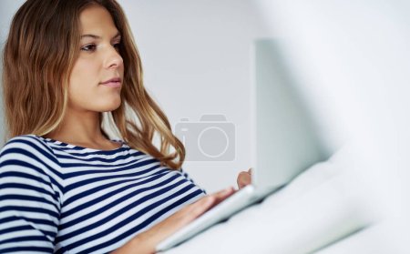 Téléchargez les photos : Je vérifie ses réseaux sociaux. une jolie jeune femme utilisant un ordinateur portable assis sur un canapé à la maison - en image libre de droit