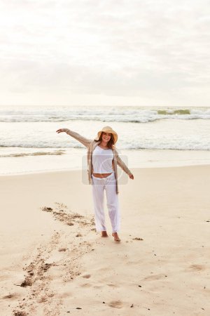 Photo for I find this to be the most relaxing season. a young woman standing with her arms outstretched at the beach - Royalty Free Image