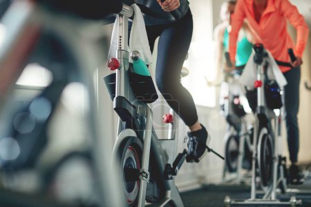 Fitness, legs and exercise bike with people in a gym for a cardio or endurance spinning class workout. Health, wellness and energy with a sporty athlete group training or cycling in a sports center.