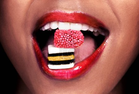 Téléchargez les photos : Les lèvres rouges en disent long. une femme méconnaissable posant avec des bonbons de réglisse dans sa bouche - en image libre de droit