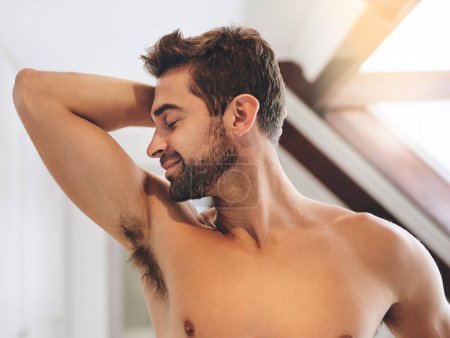 Photo for I love feeling and smelling fresh. a handsome young man smelling his armpits while standing in his bathroom at home - Royalty Free Image