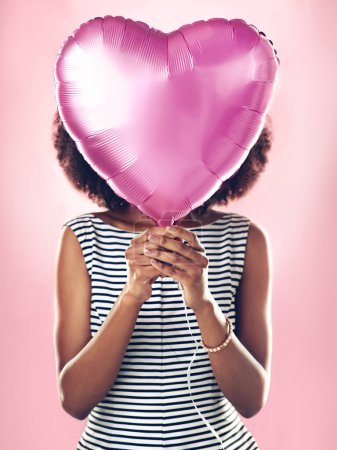 Foto de Cara de mujer cubierta con globo de corazón en estudio, fondo rosa y celebrar fiesta de cumpleaños sorpresa. Modelo de piel femenina con helio, regalo y regalo para el amor, día de San Valentín y celebración secreta. - Imagen libre de derechos
