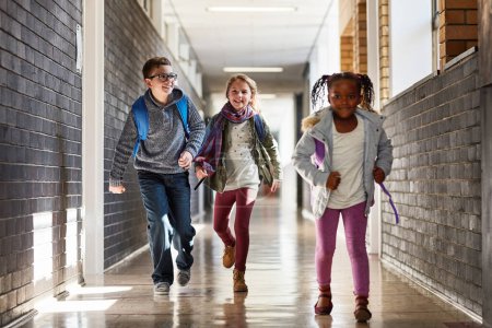 Foto de ¿Quién llegará primero a la clase? niños de primaria corriendo en el pasillo de la escuela - Imagen libre de derechos
