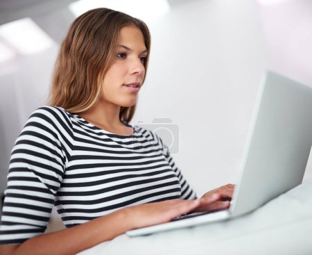 Téléchargez les photos : À la maison dans le monde en ligne. une jeune femme utilisant un ordinateur portable assis sur un canapé à la maison - en image libre de droit