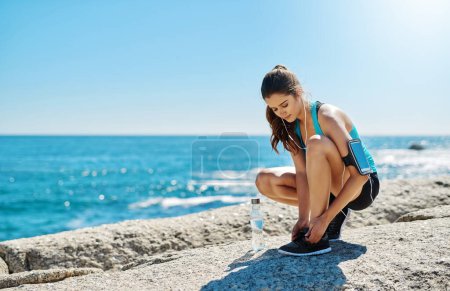 Photo for Im ready to run the world. a sporty young woman tying her shoelaces while out for a run - Royalty Free Image