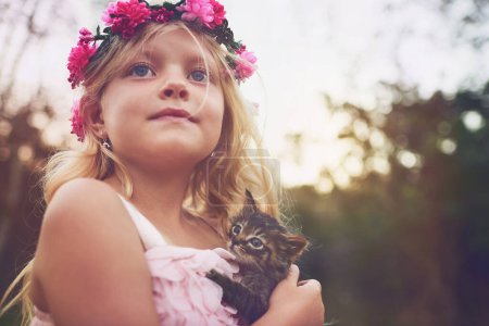 Foto de Creo que hay espacio para uno más en mi fiesta. una niña sosteniendo un gatito y mirando a la distancia mientras está de pie afuera en la naturaleza - Imagen libre de derechos