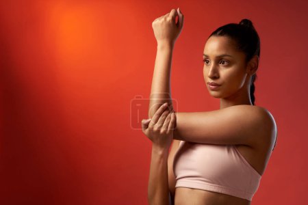 Foto de Empuja tu mente para que puedas empujar tu cuerpo también. Estudio de una joven deportista estirando los brazos sobre un fondo rojo - Imagen libre de derechos
