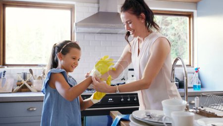Téléchargez les photos : Ces gants sont un must miel. une jeune mère affectueuse aidant sa fille à mettre des gants en caoutchouc tout en faisant la vaisselle à la maison - en image libre de droit