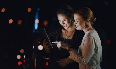 Foto de Conectado para completar su proyecto. dos empresarias que usan una tableta digital juntas fuera de una oficina por la noche - Imagen libre de derechos