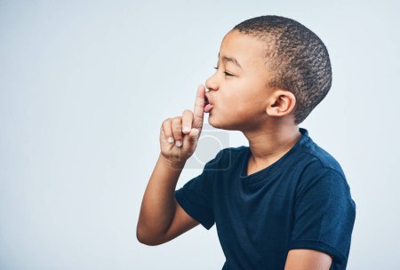 Foto de Shh... no le digas a nadie. Estudio de un lindo niño posando con el dedo en los labios sobre un fondo gris - Imagen libre de derechos