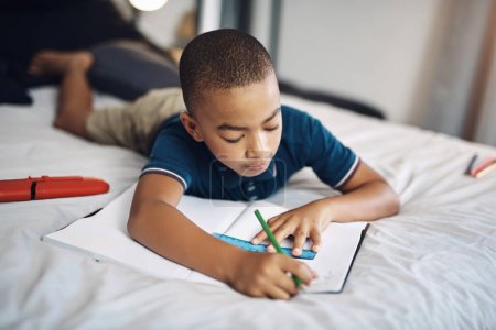 Foto de Haciendo deberes en mi lección favorita. un niño joven usando lápices para colorear mientras dibuja en casa - Imagen libre de derechos