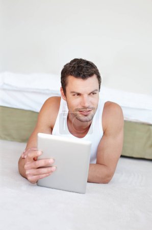 Photo for I have a world of information at my disposal. A handsome man lying on his bed working on his digital tablet - Royalty Free Image