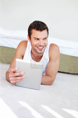 Foto de Disfrutando de la última tecnología. Un hombre guapo acostado en su cama trabajando en su tableta digital - Imagen libre de derechos