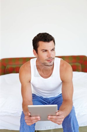 Photo for Im always connected. A man sitting on his bed holding a digital tablet - Royalty Free Image