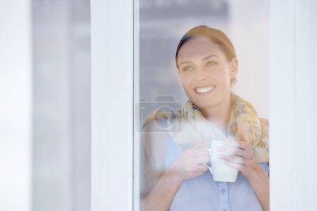 Foto de Disfrutando de su taza de café. Una joven atractiva parada junto a la ventana y tomando café - Imagen libre de derechos