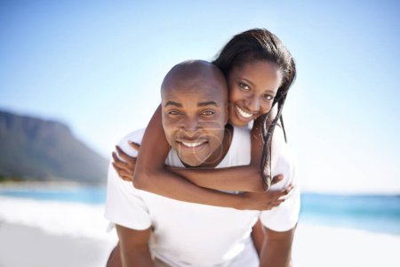 Foto de No querría pasar estas vacaciones con nadie más. Un hombre afroamericano guapo dando a su novia una vuelta a cuestas en la playa - Imagen libre de derechos