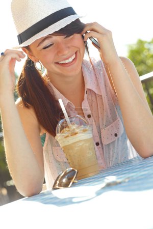 Foto de Siempre estoy en contacto con mis amigos. Una adolescente riendo mientras habla en su celular mientras está sentada en un café al aire libre - Imagen libre de derechos