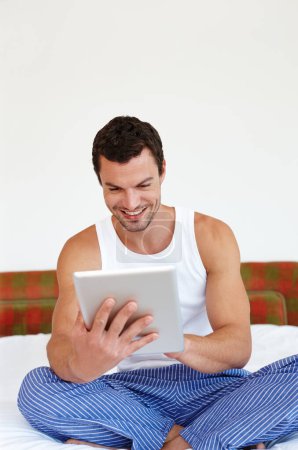 Photo for Enjoying the ease of touch technology. A man sitting on his bed holding a digital tablet - Royalty Free Image
