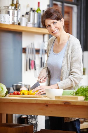 Photo for Shell wow you with her cooking. an attractive woman chopping vegetables at a kitchen counter - Royalty Free Image