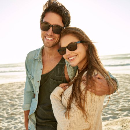 Téléchargez les photos : Soleil, mer et romantisme. Portrait d'un jeune couple amoureux portant des lunettes de soleil debout ensemble sur la plage - en image libre de droit