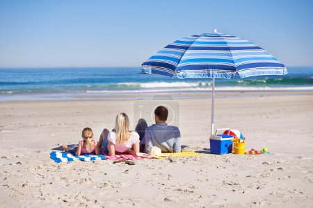 Foto de Un día perfecto juntos. Vista trasera de una familia joven y feliz sentada en la playa - Imagen libre de derechos