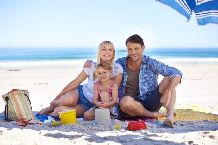 Téléchargez les photos : Regarde mon château de sable. Portrait d'une jeune famille heureuse à la plage - en image libre de droit