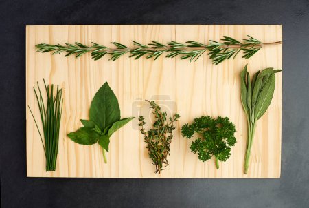 Photo for Fresh from the herb garden. High angle studio shot of basil, thyme, rosemary and other herbs lying on a chopping block - Royalty Free Image