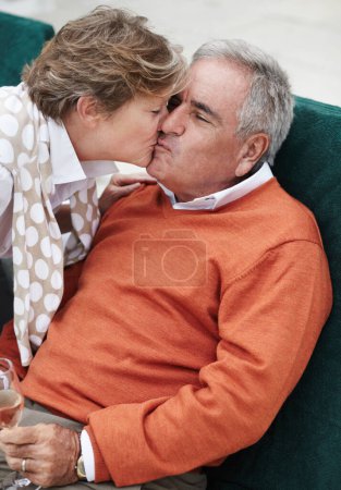 Téléchargez les photos : Lui montrant son amour. Un sénior ravi de recevoir un baiser de sa femme tout en dégustant du champagne en vacances - en image libre de droit