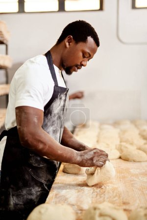 Téléchargez les photos : Je fais comme ma grand-mère me l'a appris. un boulanger masculin occupé à façonner la pâte au travail - en image libre de droit